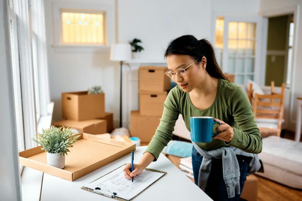 Asian woman making to do list while moving out of her apartment.