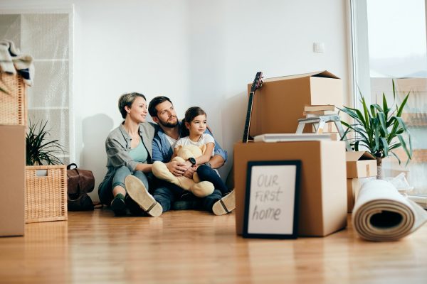 Happy parents with daughter buying fist home and relaxing on floor in their new living room.